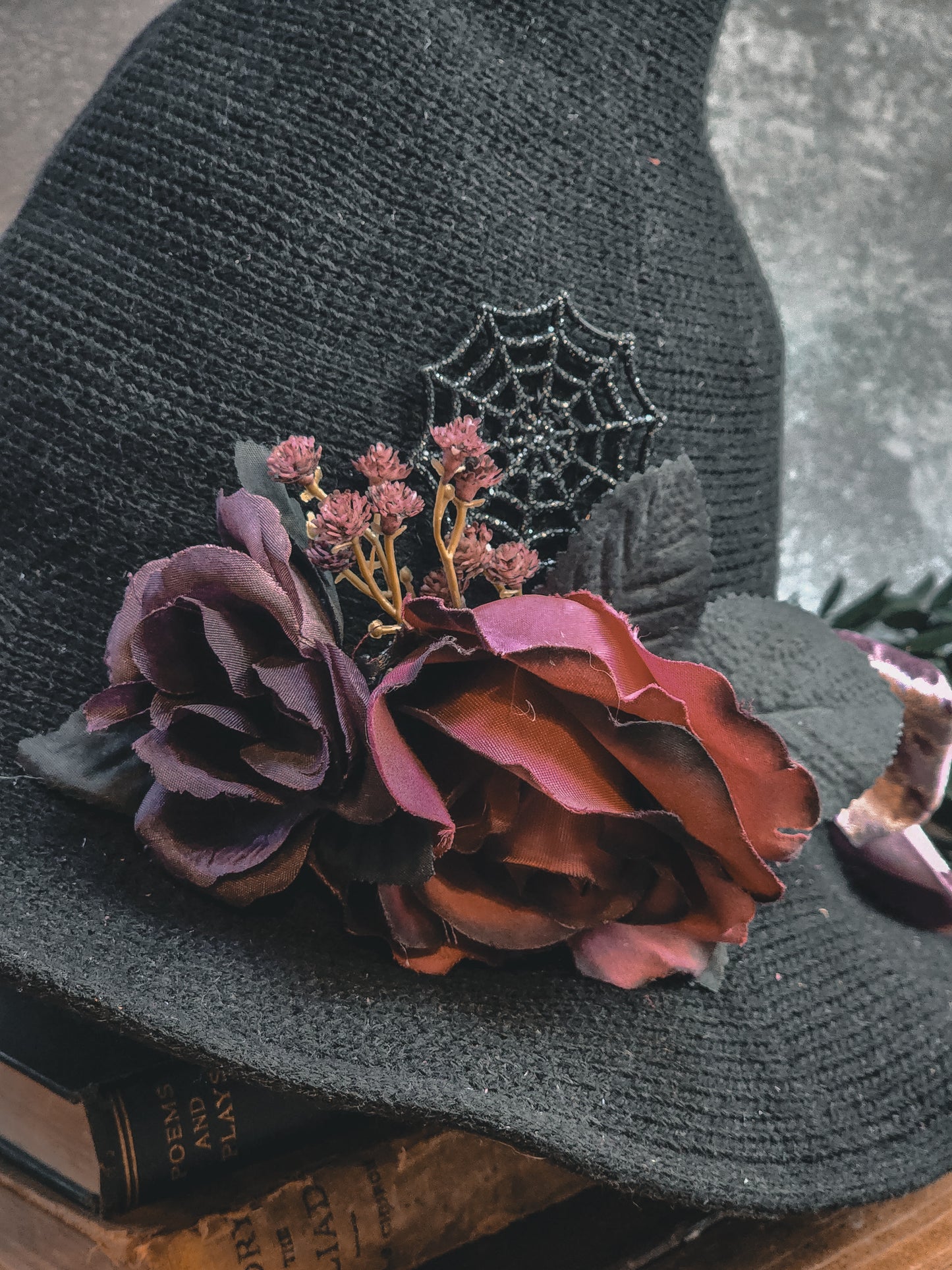 Black hat with purple flowers and a spider web design on a textured surface